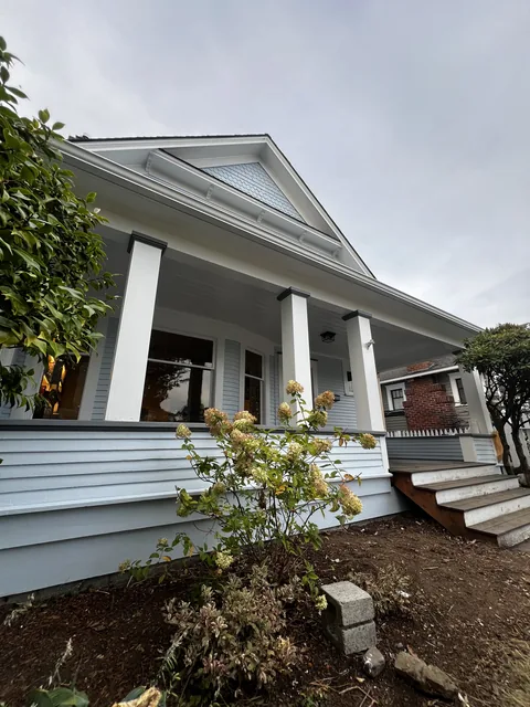Repainted front porch of a 1909 Broadway Park home in Bellingham with white square columns, charcoal caps and soft blue siding.