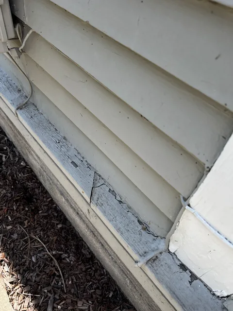 Water-table board at the base of a Bellingham home weathered to bare gray wood with moss at the foundation.