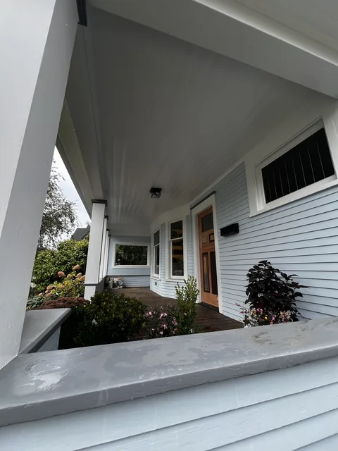 Finished front porch of a Broadway Park home in Bellingham, looking along the painted porch ceiling, white columns and soft blue siding.