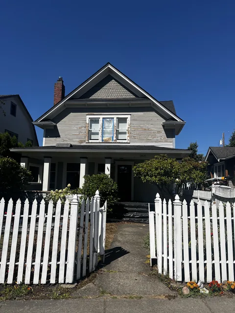 Front elevation of a 1909 Bellingham home scraped back to bare wood with windows masked and containment at the base.