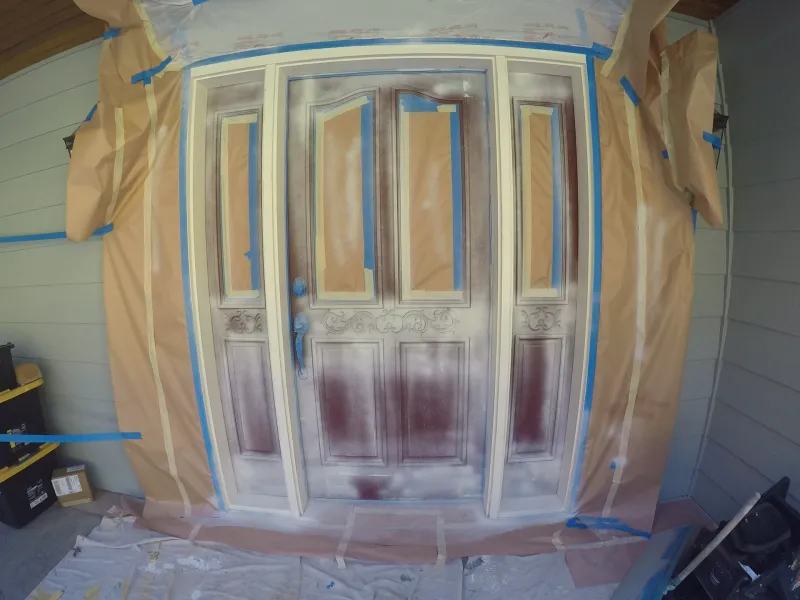 Carved front door with leaded-glass sidelights masked off for spraying, the original red finish still showing on the lower panels