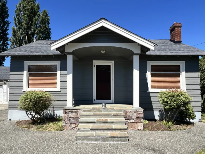 Early-1900s cedar-sided bungalow in Bellingham's Eldridge neighborhood after a full exterior repaint—medium gray body with Capital White trim and an arched entry porch.