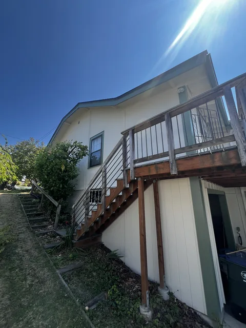 Side elevation of the finished Fairhaven repaint in Bellingham, WA showing the stair, deck framing, and refreshed siding.