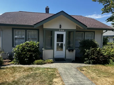 Street-facing stucco bungalow on the same Fairhaven property in Bellingham, WA, refinished with deep green trim.